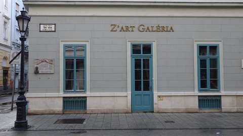 Gray gallery facade with blue doors, black lamppost at left, soft daylight