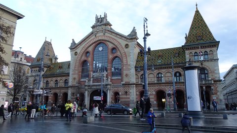 Historic covered market with glazed tile roof, pedestrians and cars under a cloudy sky