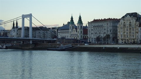 White suspension bridge and green-spired church across the river, historic buildings, evening light