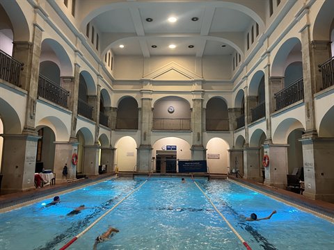 Swimmers in a historic indoor pool with arches under artificial light