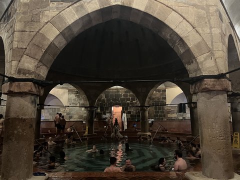 People bathing in thermal pool under stone arches, warm indoor light