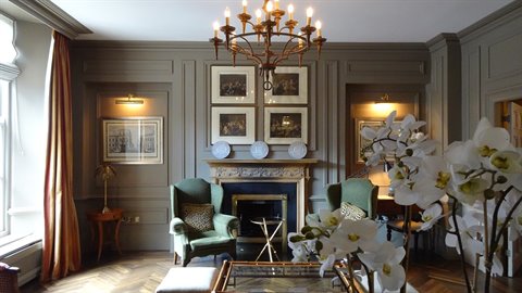 Elegant drawing room with marble fireplace, green armchairs, white orchids in foreground and brass chandelier