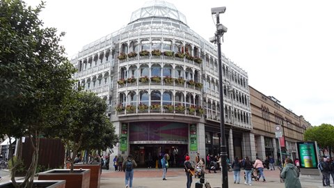 Glass building with dome and flower boxes, pedestrians below, soft overcast light