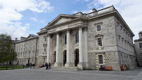 Stone building with classical columns, people sitting on steps, cloudy daylight