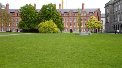 Green lawn in front of red brick building, daylight, spring trees