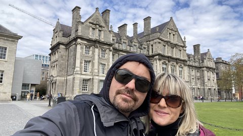 Couple taking a selfie in front of a historic stone building, cloudy daylight