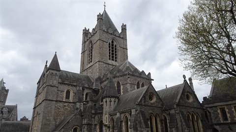 Grey stone Gothic cathedral under cloudy sky, central tower with spires and side trees