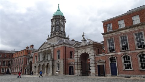 Tourists walk in the courtyard of a historic red-brick building with a green clock tower