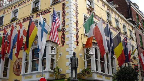 Bronze statue in front of yellow pub with international flags, diffuse light