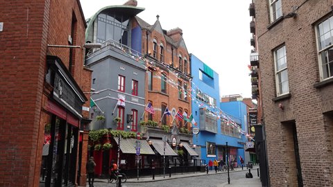 Pedestrian street with colorful buildings, gray and blue facades, flags, diffused light, people walking