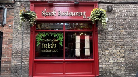 Red facade of an Irish restaurant on brick wall, daylight, hanging flower baskets