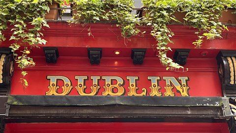 Golden sign on red pub facade covered with ivy, daylight