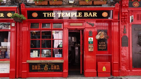 Red pub facade with gold signs, open door, daytime light