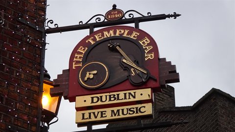Wooden and iron pub sign with fiddle, lit lantern against red brick