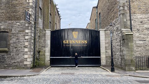 Traveler in front of the large black Guinness brewery gate between stone walls