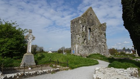 Old Celtic stone cross beside monastic ruins on grass under a cloudy sky