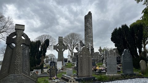 Old graveyard with Celtic stone crosses and round tower under a cloudy sky