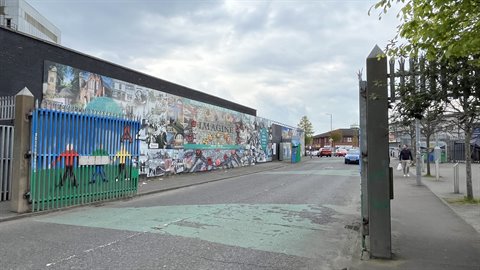 Open green gate in front of a long wall covered with colorful murals, soft light