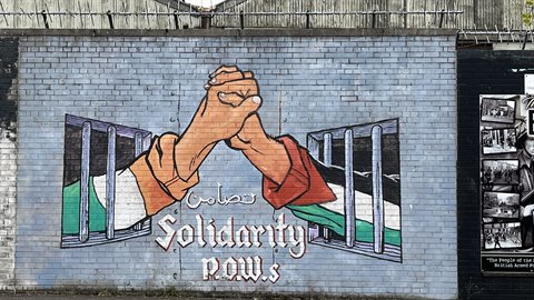 Mural on grey brick wall, joined fists breaking through prison bars