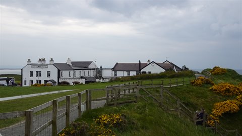 White buildings on green hillside, wooden fence, yellow gorse, cloudy sky