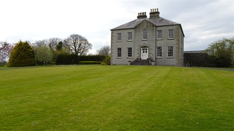 Old stone manor house in front of green lawn, diffused light