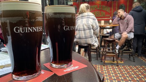 Two pints of Guinness on a wooden table in a busy pub