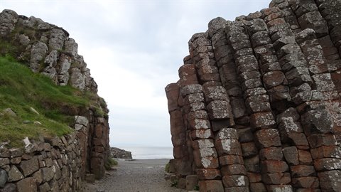 Basalt columns open onto a path toward the sea under a cloudy sky