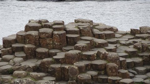 Hexagonal basalt columns on the shore, soft daylight, grey sea in background