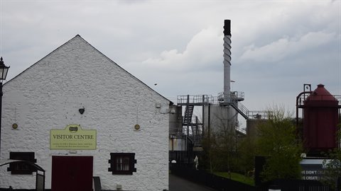 White visitor centre building with distillery plant and chimney under cloudy sky