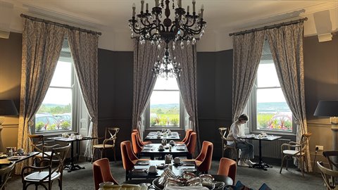 Tea room with crystal chandeliers, orange armchairs, woman seated by window, natural light