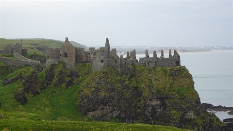 Medieval castle ruins on a green cliff above the sea under grey sky