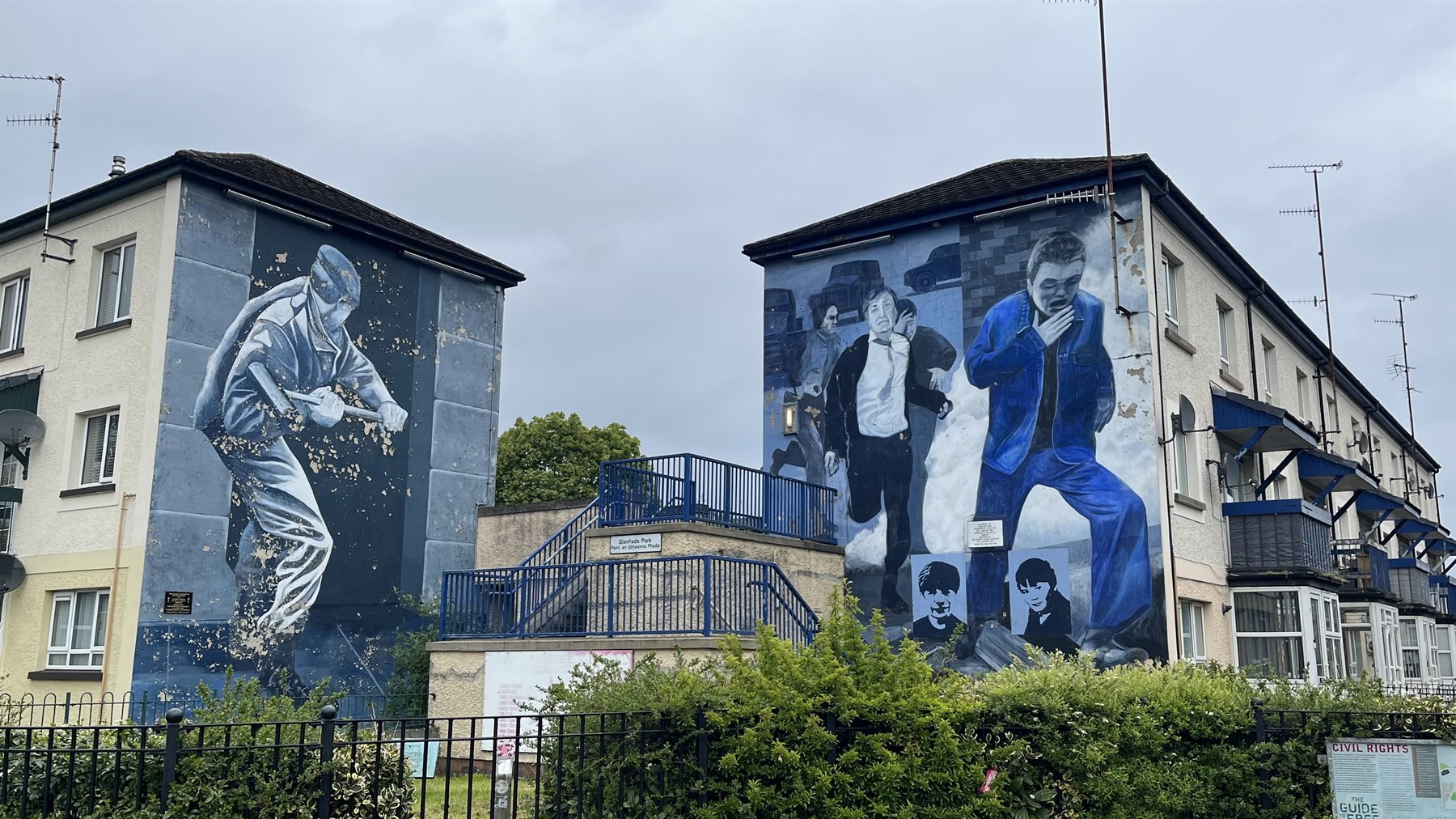 Murals painted on the sides of residential buildings, diffused light, hedges along the fence