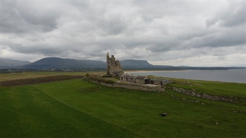 Old stone castle on green coast beneath heavy cloudy skies