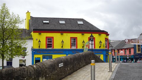 Yellow and red pub facade beside stone bridge, grey cloudy sky