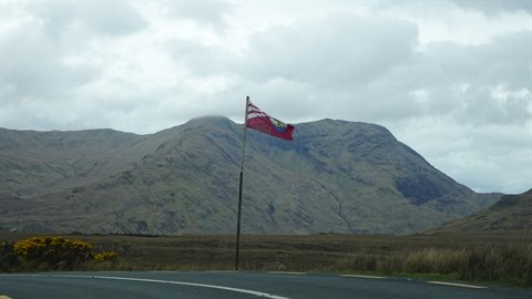 Red flag on a pole along a road, brown mountains under cloudy sky