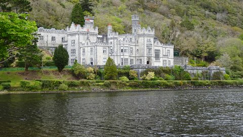 Grey stone castle by a lake shore, green woodland behind, soft daylight