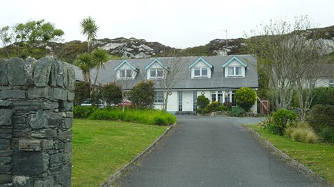 Rural house in light stone with blue roofs, entrance driveway, diffused light, rocky hills