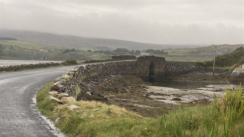 Coastal road beside an old stone bridge under cloudy sky