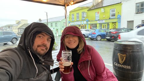 Couple under a canopy with a Guinness pint, rainy street and colorful buildings behind