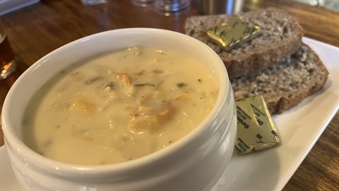 Creamy seafood chowder in white bowl with brown bread and butter on wooden table