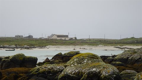 White houses along the coast under grey sky, mossy rocks and boat in foreground