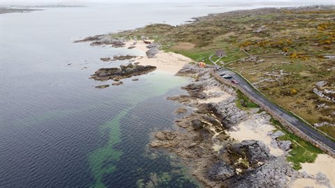 Sand, rocks and coastal road under soft light, calm ocean on an overcast day