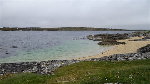 Turquoise bay between grey rocks and sand, cloudy sky, soft diffused light