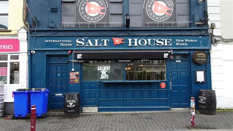 Blue pub facade with signs, bins and barrels outside, soft daylight