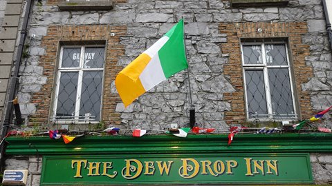 Irish flag flying over grey stone facade with green pub sign