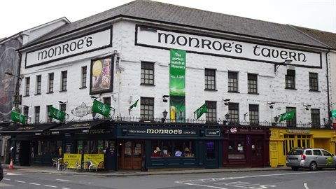 white pub facade with green flags, daylight, parked car, corner street