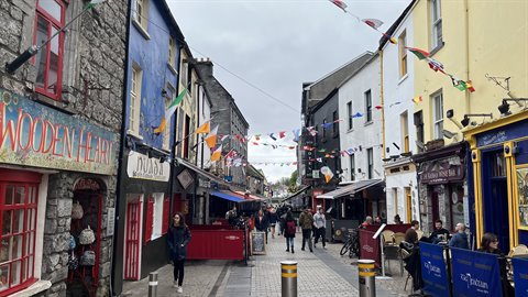Pedestrian street with colourful facades and flags, people walking under grey sky