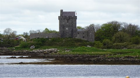 Old stone castle on grassy shore, cloudy sky, rippling water in foreground