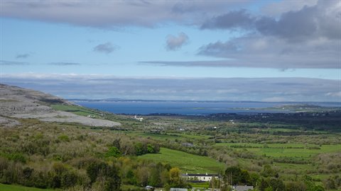Green rolling hills and blue bay under cloudy sky, rural Ireland