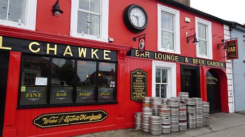 Red pub with gold lettering, black clock and metal beer kegs lined on the street